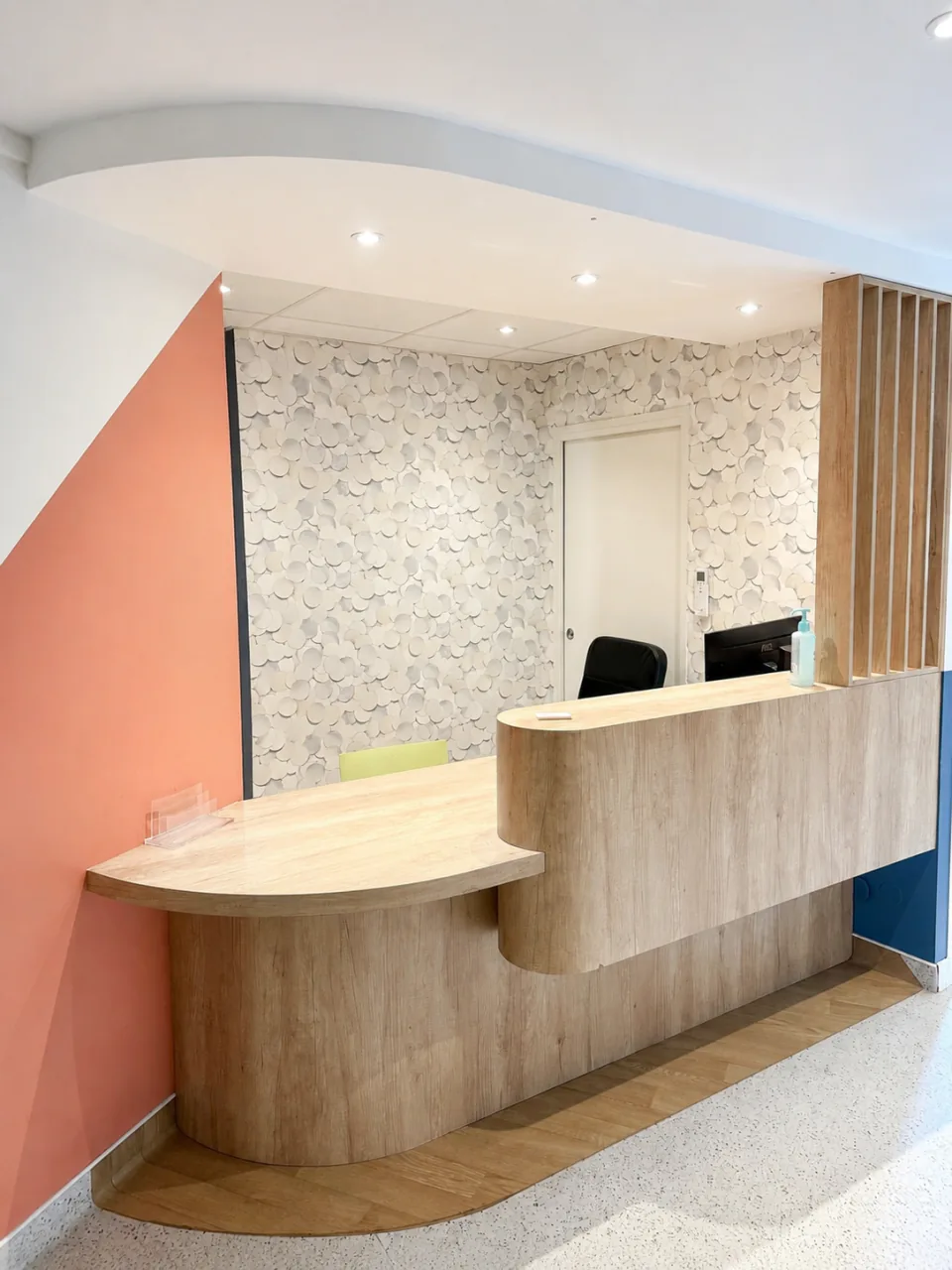 Le comptoir d’accueil arrondi en bois, devant le mur pêche du cabinet.