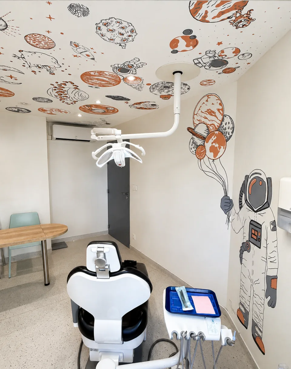 La seconde salle de soins du cabinet, avec un fauteuil et des astronautes et planètes peints sur les murs et le plafond.