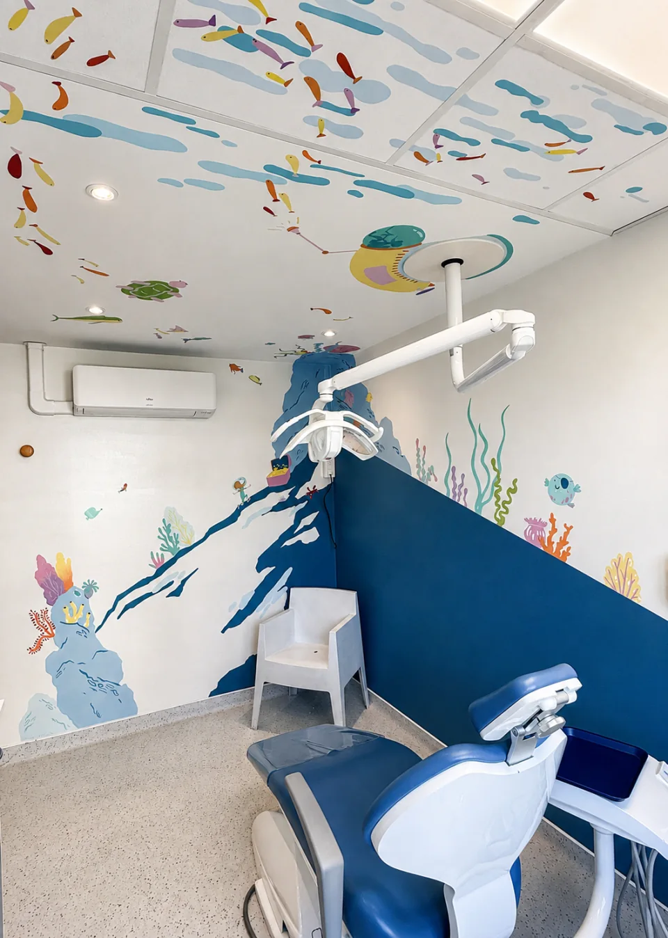 Une salle de soins du cabinet, avec un fauteuil bleu et des poissons peints sur les murs et le plafond.